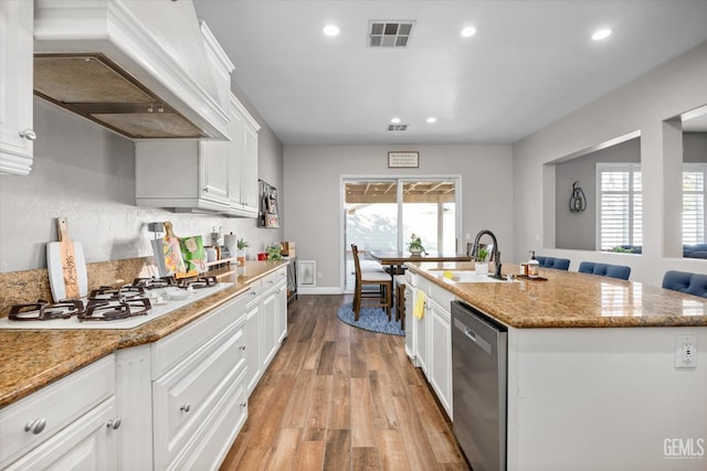 kitchen with light wood finished floors, custom range hood, stainless steel dishwasher, white gas cooktop, and a sink