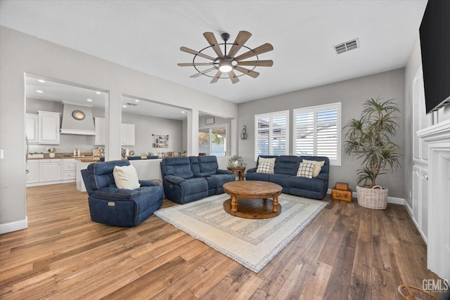 living area featuring ceiling fan, light wood-style flooring, visible vents, and baseboards