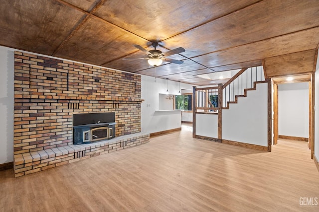 unfurnished living room with light hardwood / wood-style flooring, a wood stove, ceiling fan, and wooden ceiling