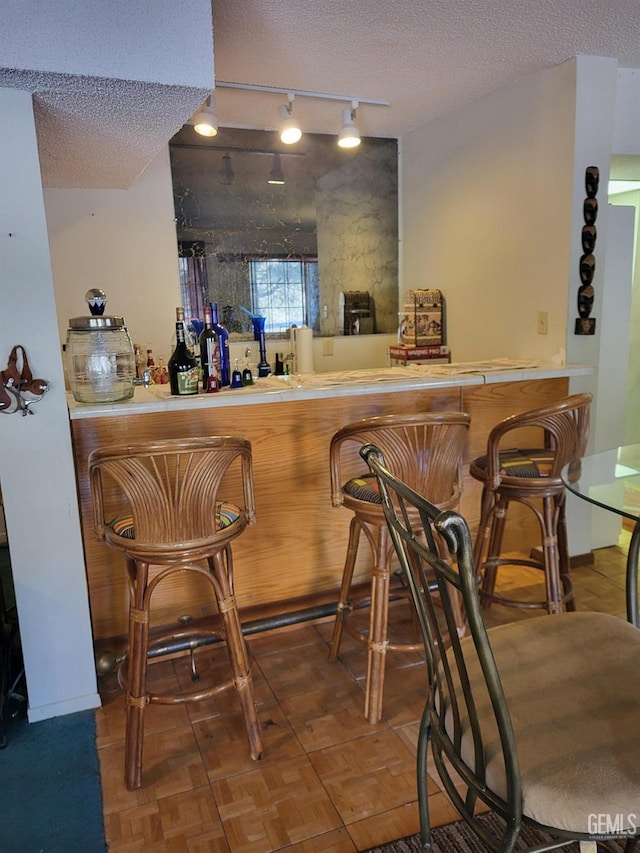 bar with indoor bar, baseboards, rail lighting, and a textured ceiling
