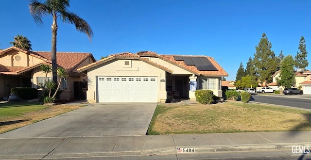 ranch-style home featuring driveway, a garage, stucco siding, roof mounted solar panels, and a tiled roof