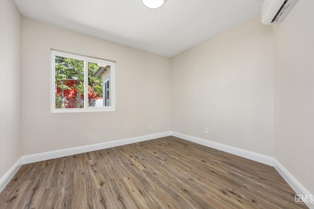 unfurnished room featuring a wall unit AC, wood finished floors, and baseboards