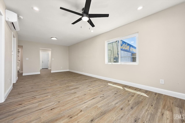 empty room with a wall unit AC, ceiling fan, light wood-style floors, baseboards, and recessed lighting