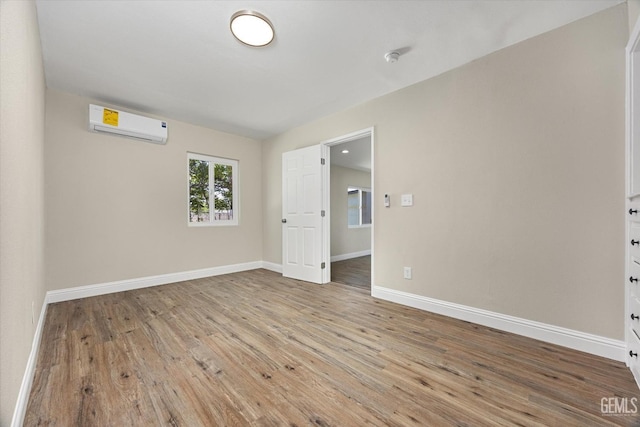 empty room featuring a wall mounted air conditioner, wood finished floors, and baseboards