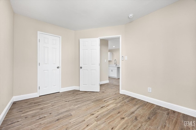 unfurnished bedroom with wood finished floors, baseboards, and a sink