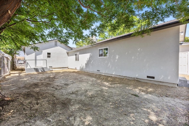 back of property featuring crawl space, stucco siding, and fence