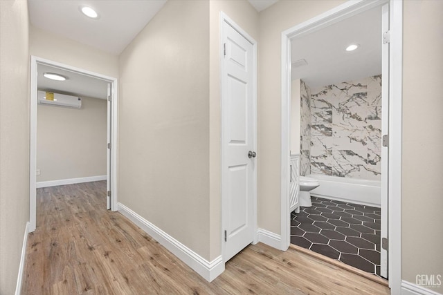 corridor featuring an AC wall unit, light wood finished floors, recessed lighting, and baseboards