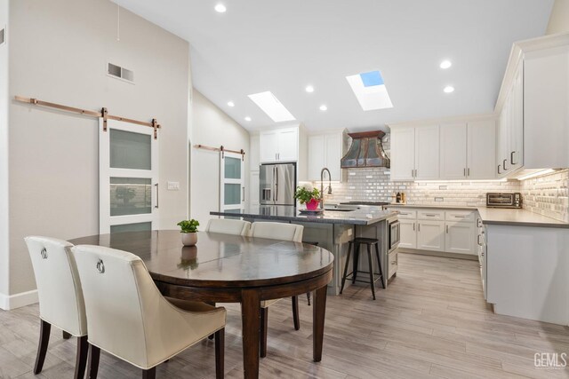 8220 Birmingham St, Bakersfield, CA 93311 - dining area featuring a barn door, vaulted ceiling, light wood-style floors, a skylight, and recessed lighting