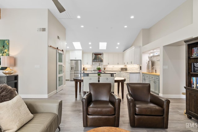 8220 Birmingham St, Bakersfield, CA 93311 - living room featuring a barn door, light wood finished floors, recessed lighting, vaulted ceiling, and baseboards