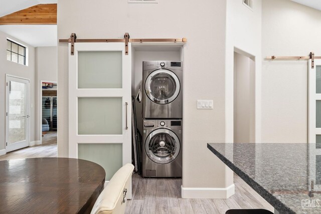 8220 Birmingham St, Bakersfield, CA 93311 - washroom featuring a barn door, stacked washer / dryer, light wood-style floors, and baseboards