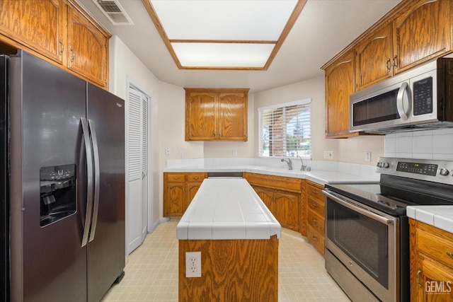 10200 Cheyenne Dr, Bakersfield, CA 93312 - kitchen with stainless steel appliances, tile countertops, a center island, brown cabinets, and light floors