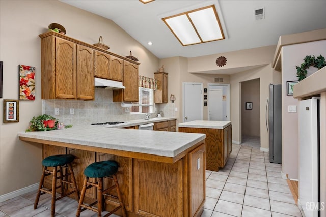 kitchen with white appliances, a breakfast bar, tasteful backsplash, light tile patterned flooring, and kitchen peninsula