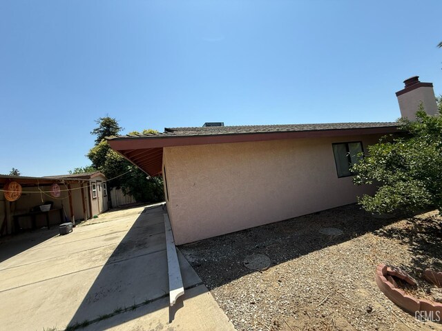 1328 Malerbi Ct, Bakersfield, CA 93307 - view of side of home with stucco siding, driveway, a patio area, and a chimney
