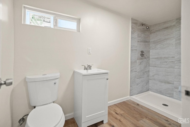 bathroom featuring hardwood / wood-style flooring, vanity, toilet, and a tile shower