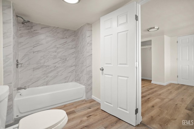 bathroom featuring wood-type flooring, tiled shower / bath combo, and toilet