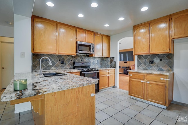 kitchen featuring kitchen peninsula, light stone countertops, black range oven, and sink