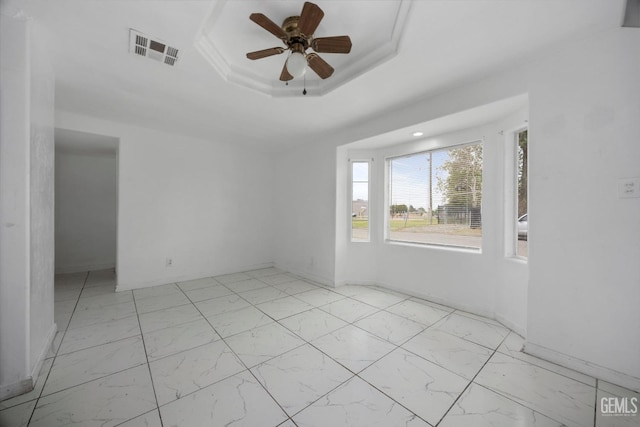 spare room with a ceiling fan, a tray ceiling, baseboards, marble finish floor, and visible vents