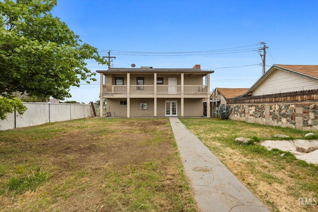 back of house with fence, a balcony, stucco siding, a chimney, and a lawn