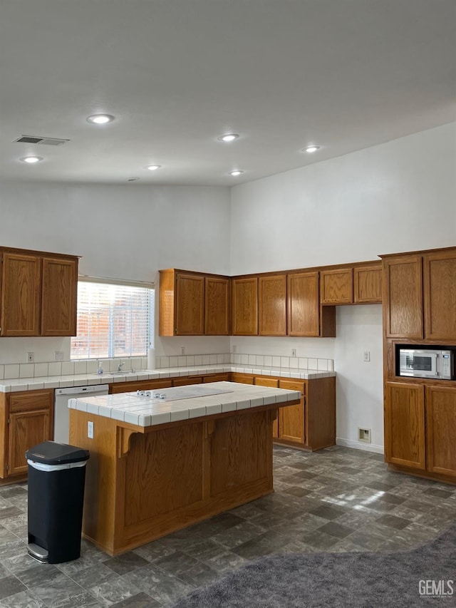 kitchen with a kitchen bar, white dishwasher, a high ceiling, a kitchen island, and tile counters