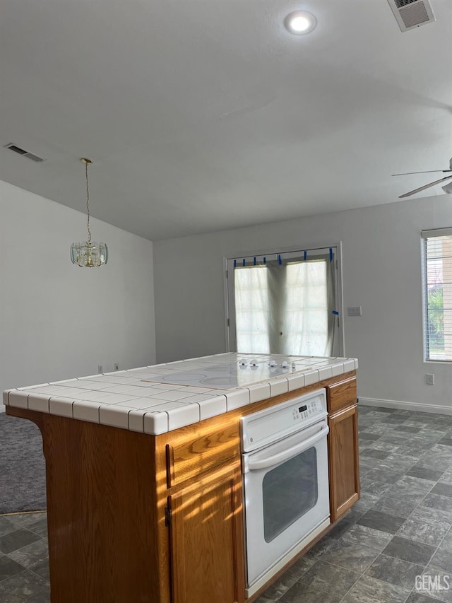 kitchen featuring a center island, white oven, ceiling fan with notable chandelier, decorative light fixtures, and tile counters