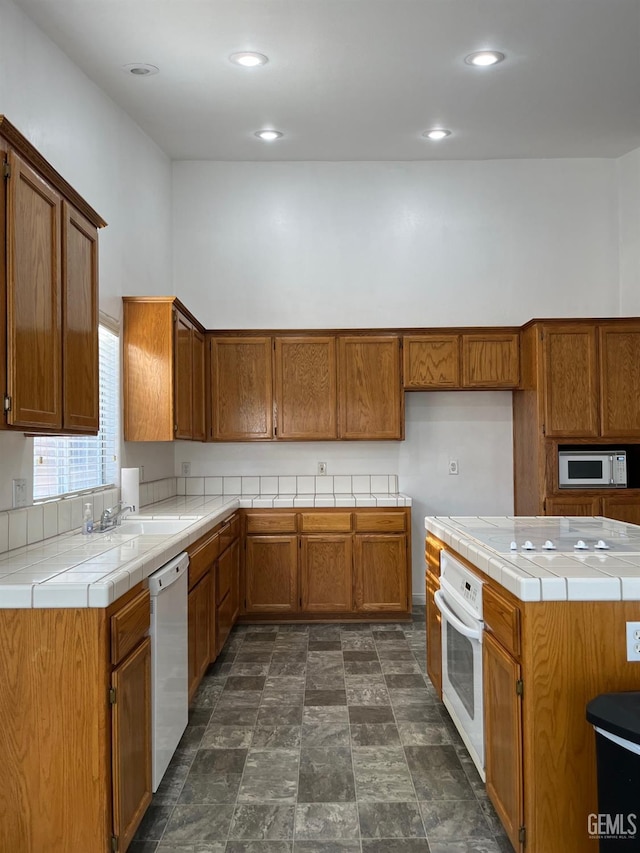 kitchen with a towering ceiling, white appliances, tile counters, and sink