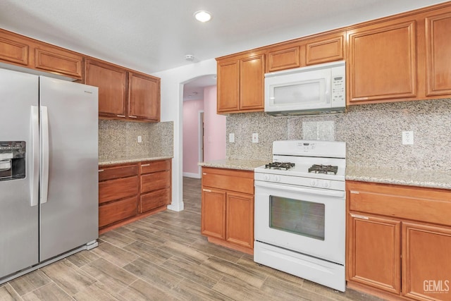 kitchen with white appliances, backsplash, light hardwood / wood-style flooring, and light stone counters