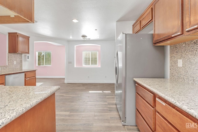 kitchen with a textured ceiling, light hardwood / wood-style floors, backsplash, light stone countertops, and appliances with stainless steel finishes