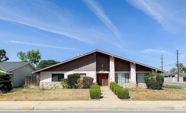 mid-century home with stone siding, stucco siding, and fence
