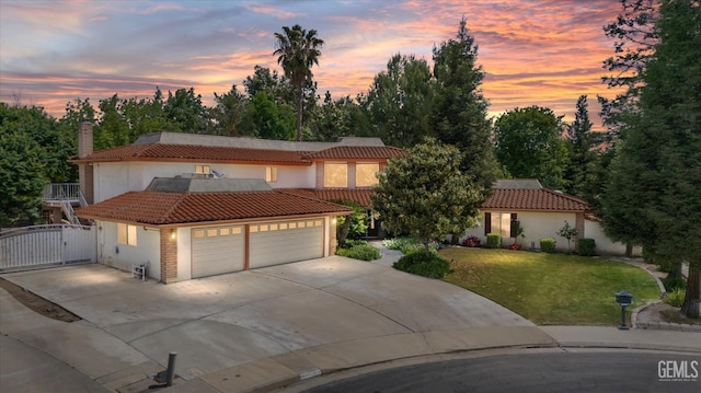 view of front of house with concrete driveway, a lawn, a tiled roof, and a gate
