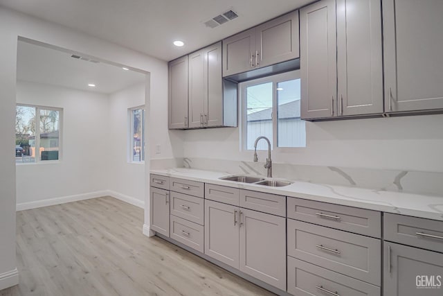 kitchen featuring gray cabinetry, a sink, visible vents, light stone countertops, and light wood finished floors