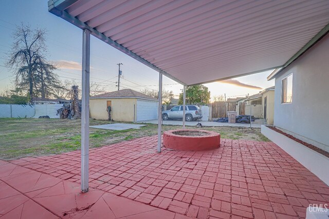 patio terrace at dusk featuring a fire pit, fence, and an outbuilding