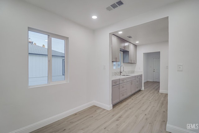 kitchen with light wood finished floors, baseboards, gray cabinets, and a sink