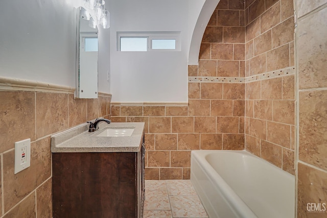 full bathroom with a wainscoted wall, a bathing tub, tile walls, and vanity