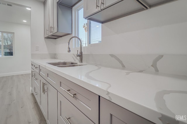 kitchen with light wood finished floors, visible vents, a sink, light stone countertops, and baseboards