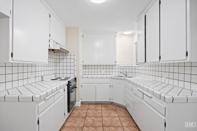 kitchen with extractor fan, white cabinetry, black range with electric stovetop, and tile counters