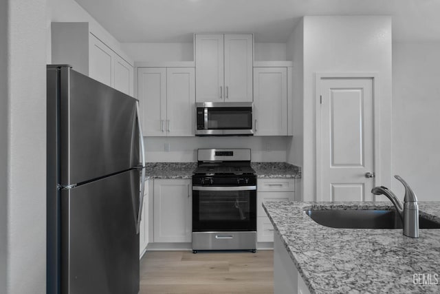 8407 Seth Alexander Way, Bakersfield, CA 93306 - kitchen with appliances with stainless steel finishes, a sink, light wood-style flooring, light stone countertops, and white cabinets