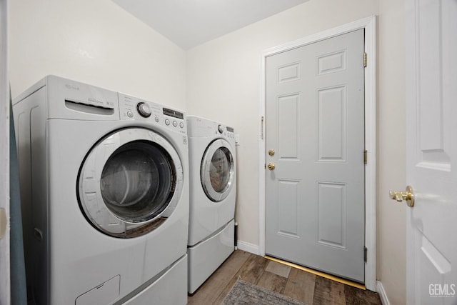 clothes washing area featuring baseboards, separate washer and dryer, wood finished floors, and laundry area