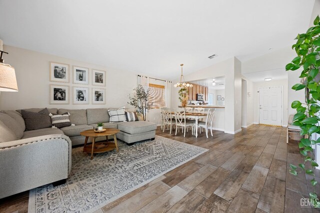 living area featuring visible vents, wood finished floors, an inviting chandelier, baseboards, and vaulted ceiling