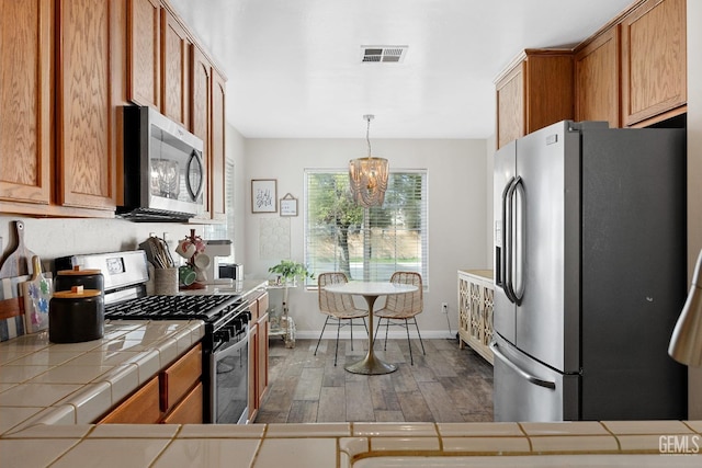 kitchen featuring visible vents, brown cabinets, tile countertops, stainless steel appliances, and dark wood-style flooring