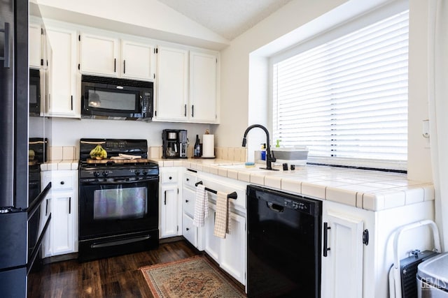 kitchen with white cabinetry, black appliances, lofted ceiling, and tile countertops