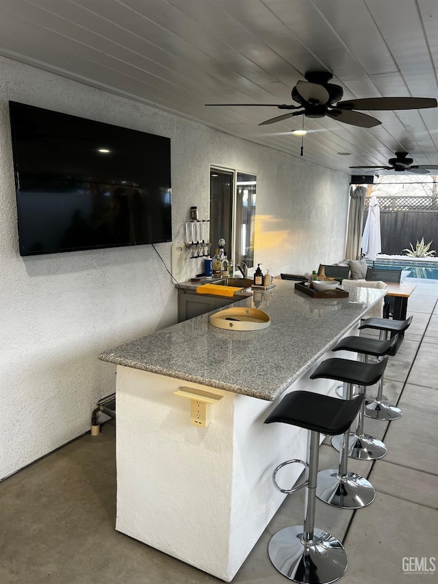 kitchen featuring concrete flooring, ceiling fan, wooden ceiling, and a kitchen bar