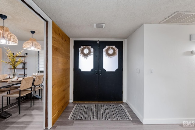 entryway with a textured ceiling, wood finished floors, visible vents, and baseboards