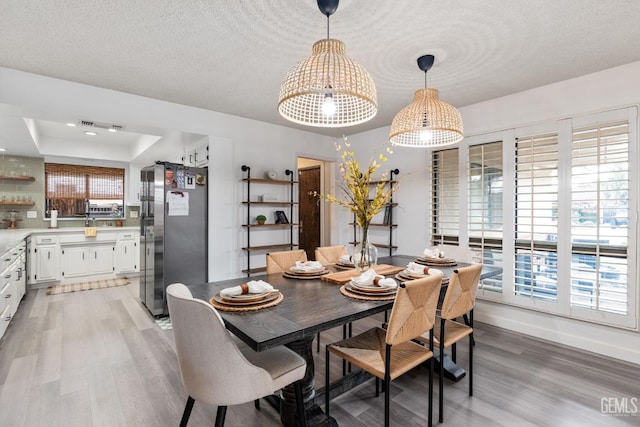 dining room with light wood-style flooring, baseboards, a raised ceiling, and a textured ceiling