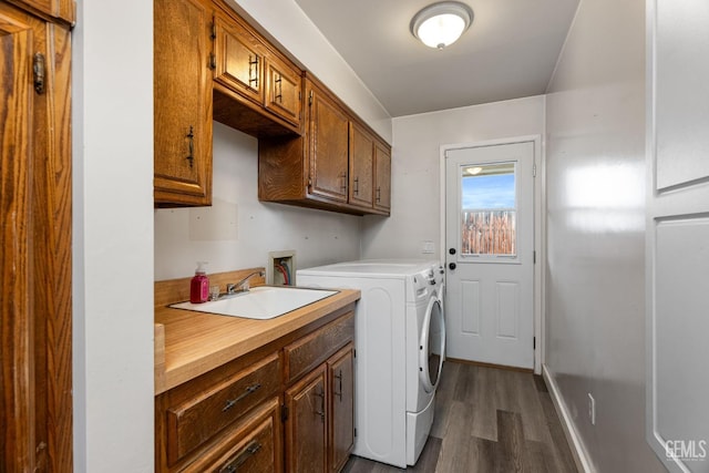 washroom featuring cabinet space, baseboards, dark wood-type flooring, washing machine and clothes dryer, and a sink