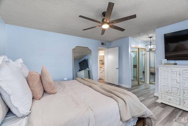 bedroom featuring visible vents, connected bathroom, a textured ceiling, wood finished floors, and ceiling fan with notable chandelier