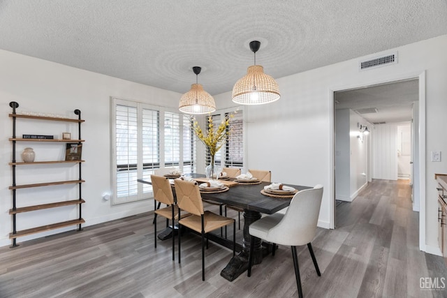 dining space featuring baseboards, a textured ceiling, visible vents, and wood finished floors