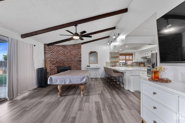 bedroom with light wood-style floors, a fireplace, a textured ceiling, and beamed ceiling