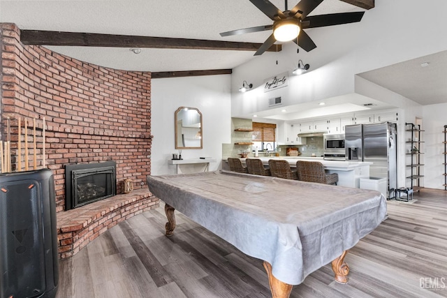 recreation room with a textured ceiling, lofted ceiling with beams, a fireplace, visible vents, and light wood finished floors