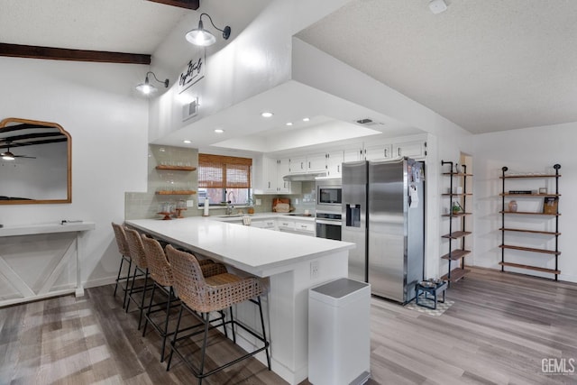 kitchen with backsplash, appliances with stainless steel finishes, light wood-style floors, white cabinets, and a peninsula