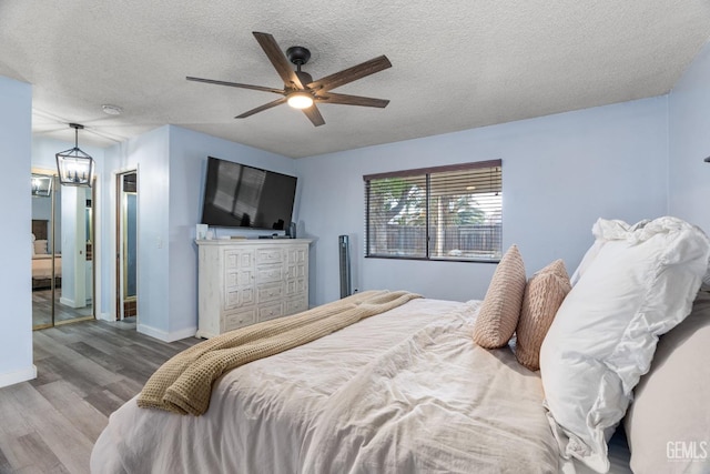 bedroom with a textured ceiling, baseboards, wood finished floors, and ceiling fan with notable chandelier